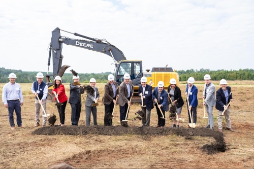 group of key stakeholders in hard hats using shovels to toss dirt in a symbolic ground breaking gesture